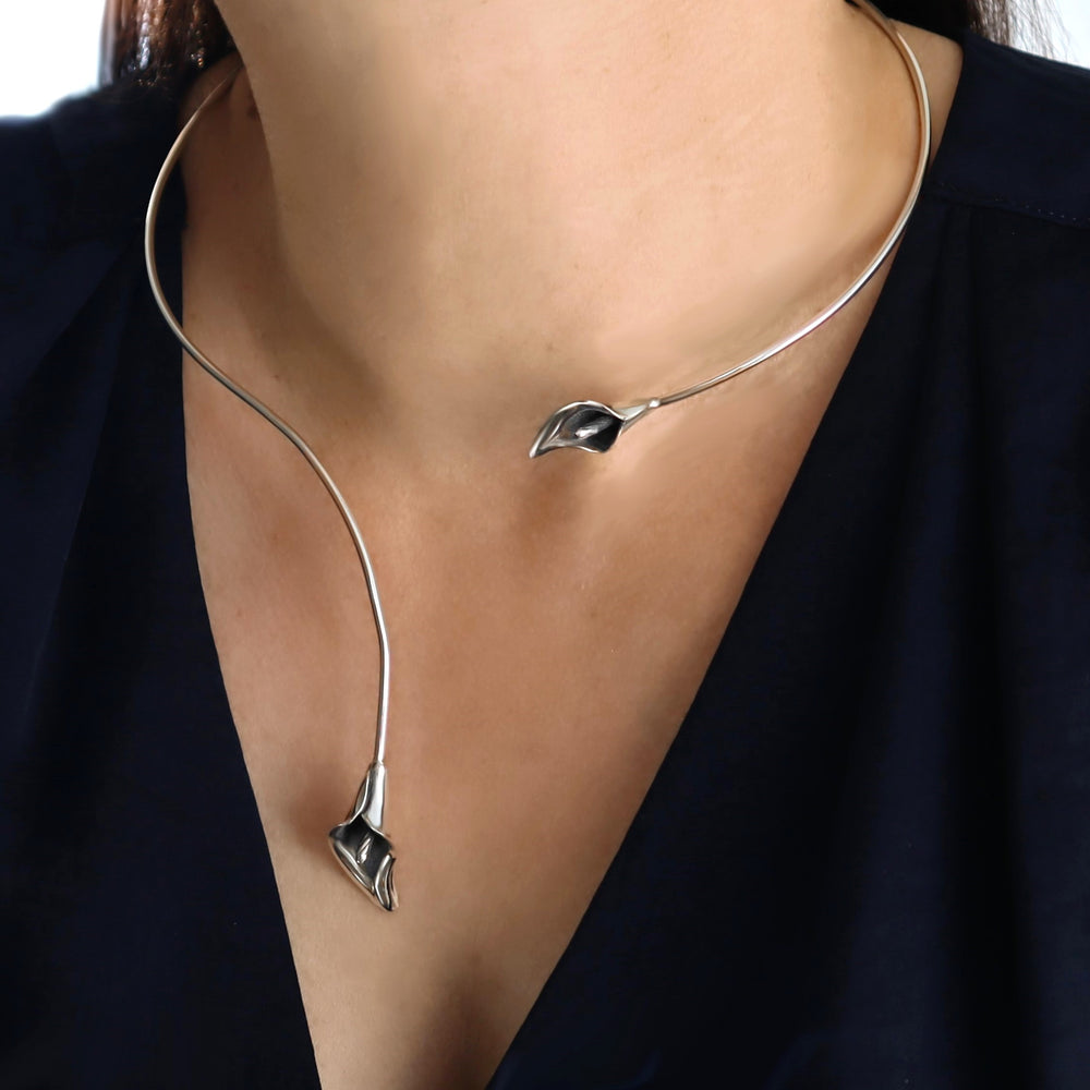 A calla lily design necklace choker in silver worn by a woman with a blue blouse.