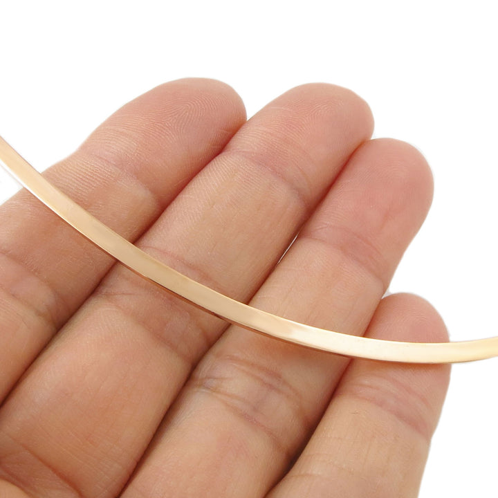 Ladies polished solid copper rigid choker torque necklace held between fingers against a white background