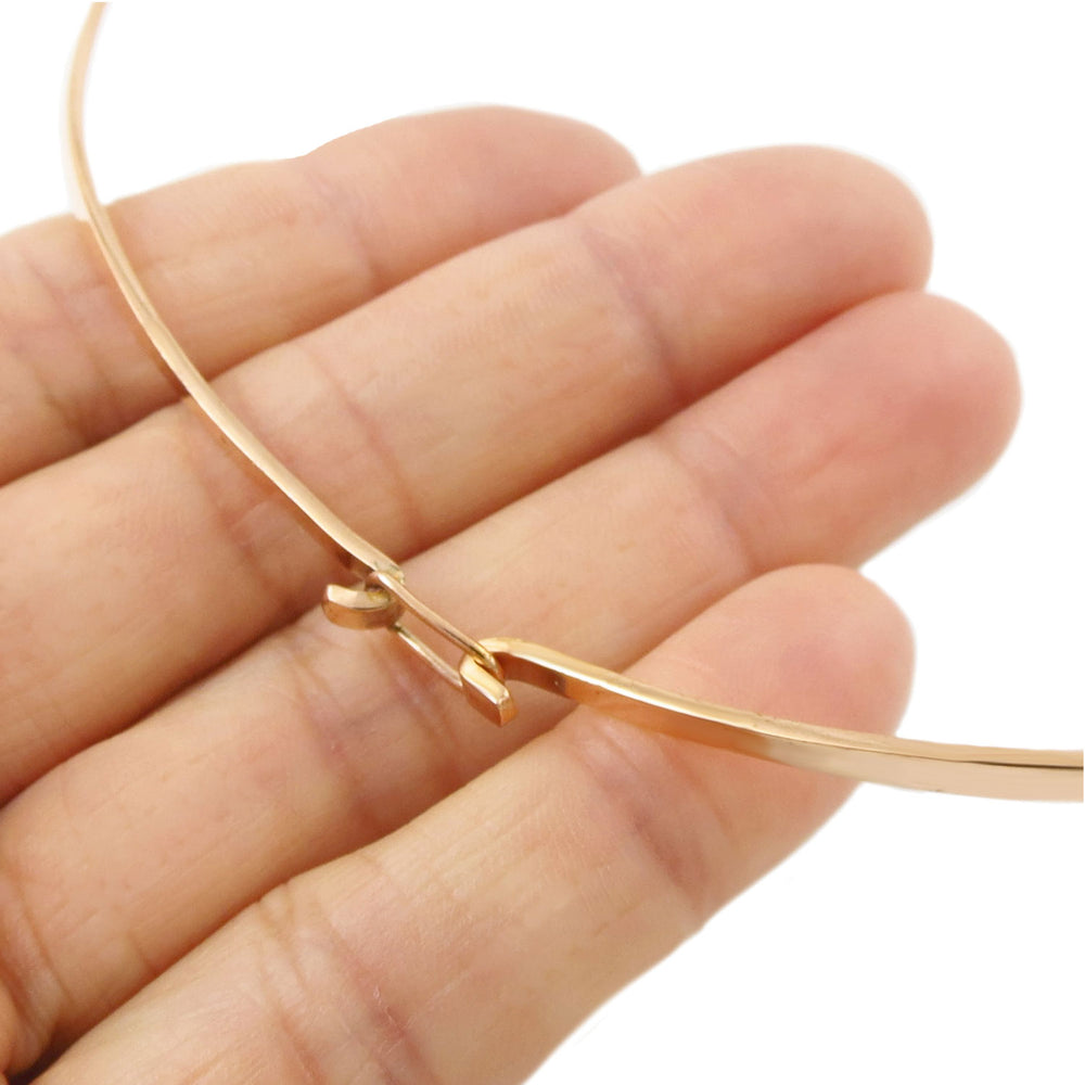Polished copper choker necklace for women with a hook fastener held between fingers on a white background