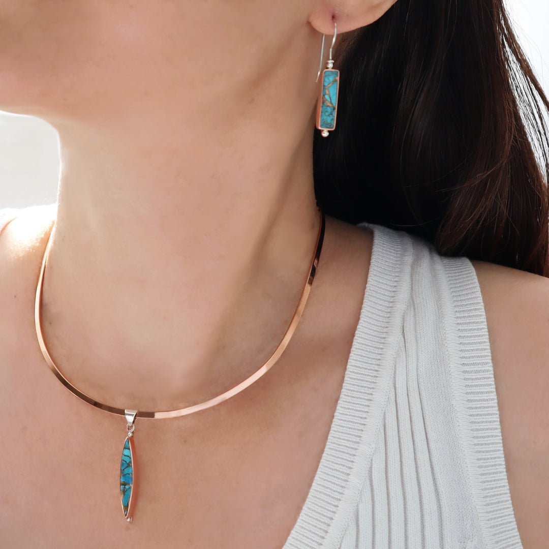 Close-up of a person wearing turquoise pendant earrings and a copper choker necklace.