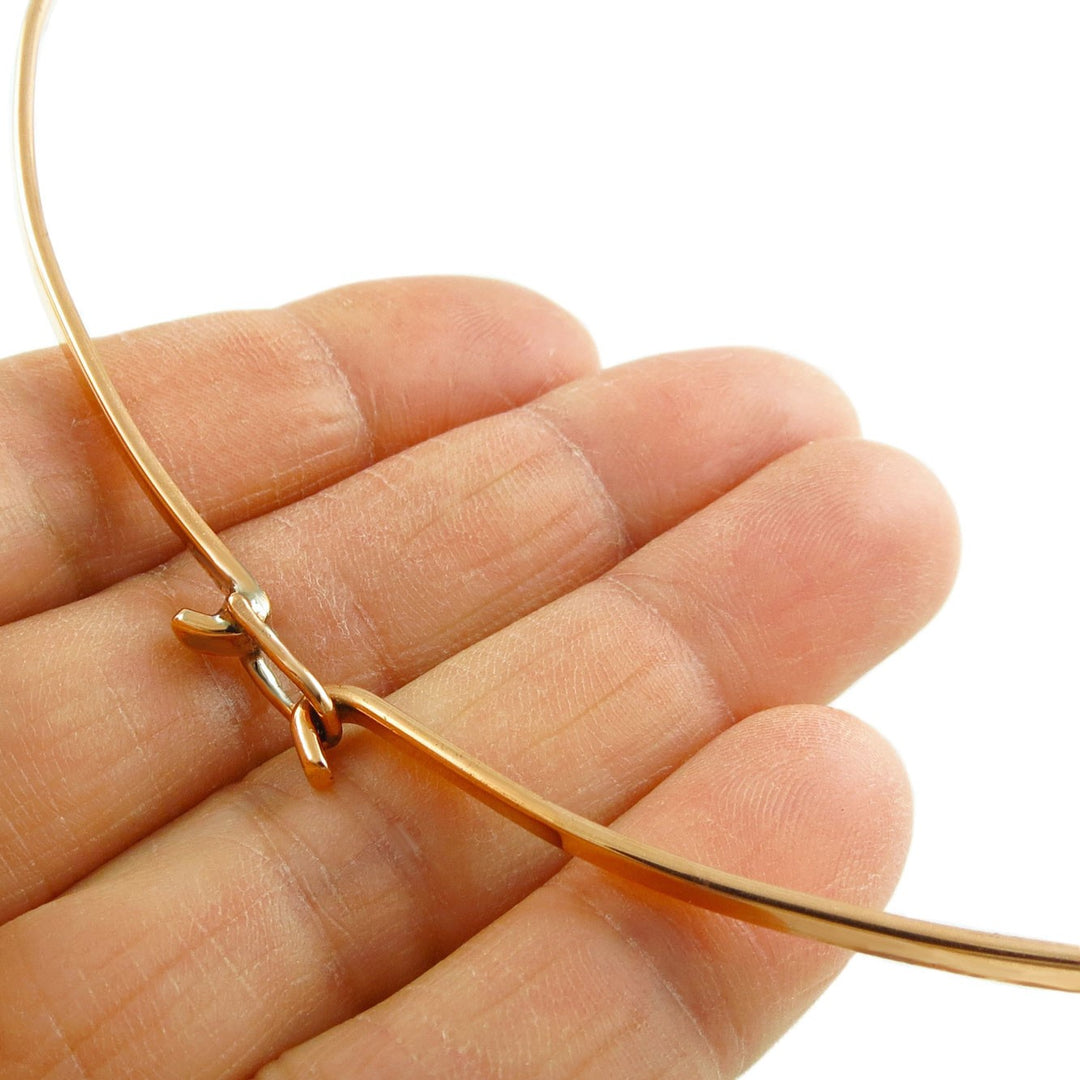 Women's copper choker necklace with a hook faastening being held between fingers on a white background