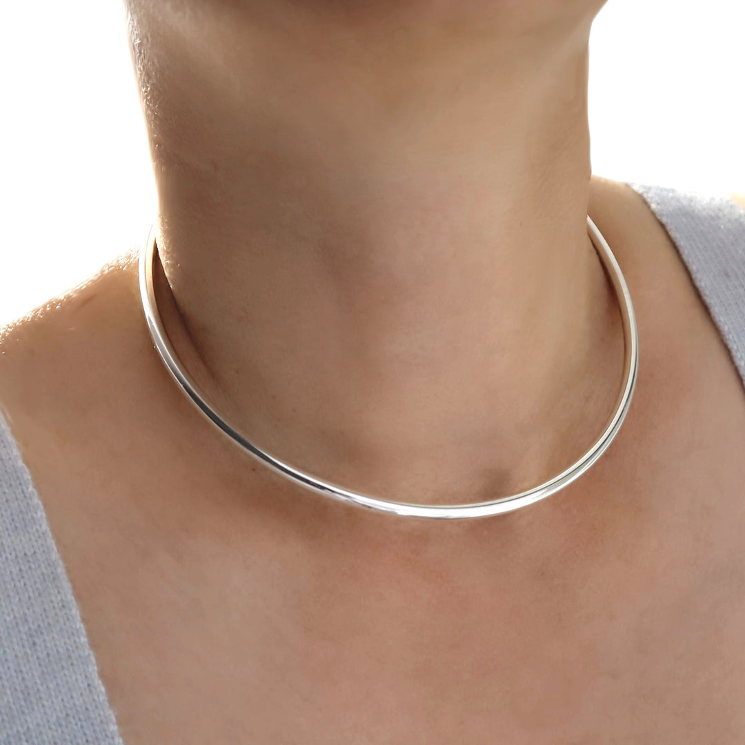 Silver choker necklace on a person's neck with a neutral background