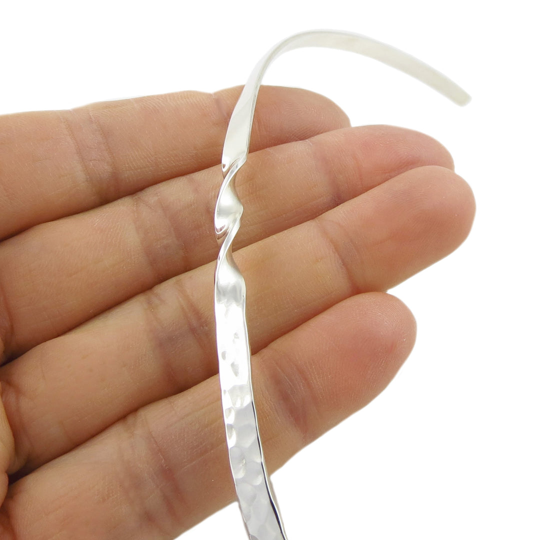 Silver choker torc held between fingers against a white background