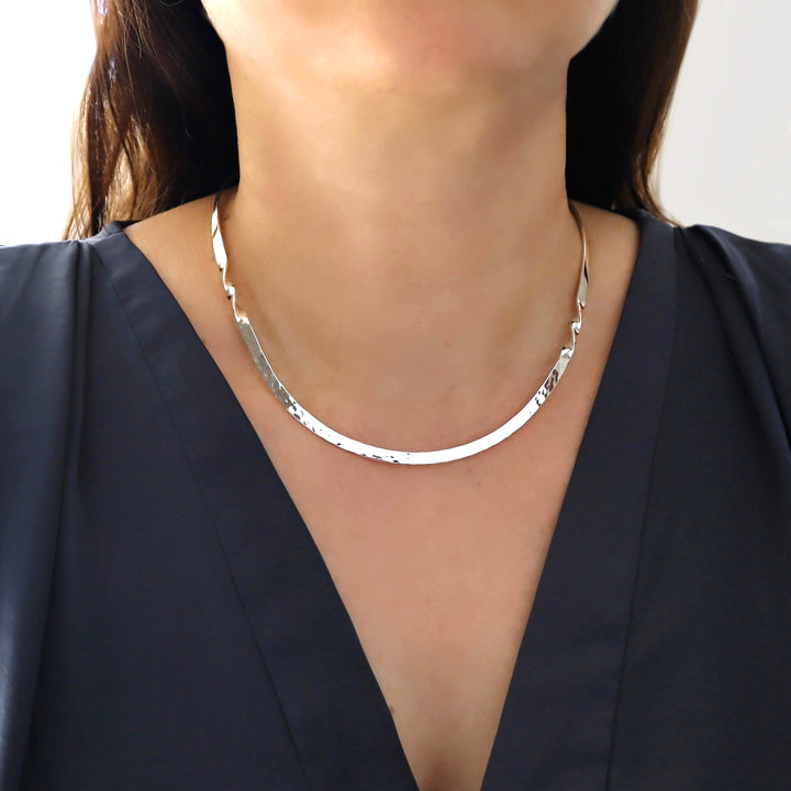 Silver choker style necklace worn by a person against a neutral background