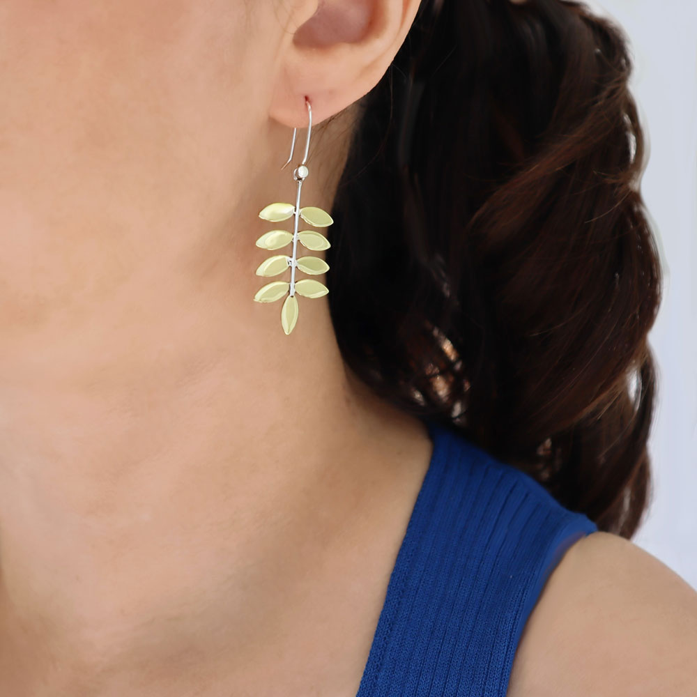 A long gold and sterling silver tree leaf design drop earring worn by a woman with dark hair wearing a royal blue top.