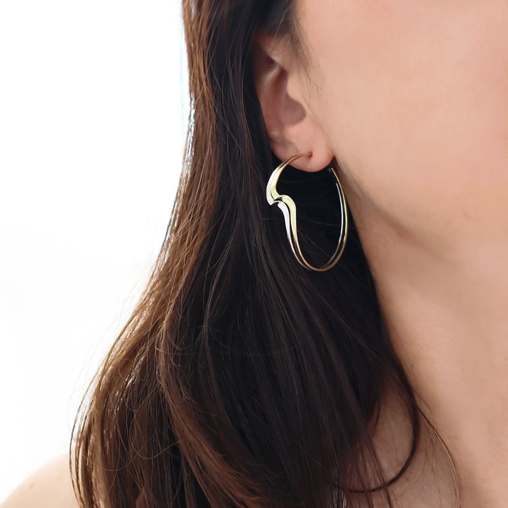 A large, sculpted hoop earring in 925 silver and gold mixed metals worn by a woman with long dark hair.