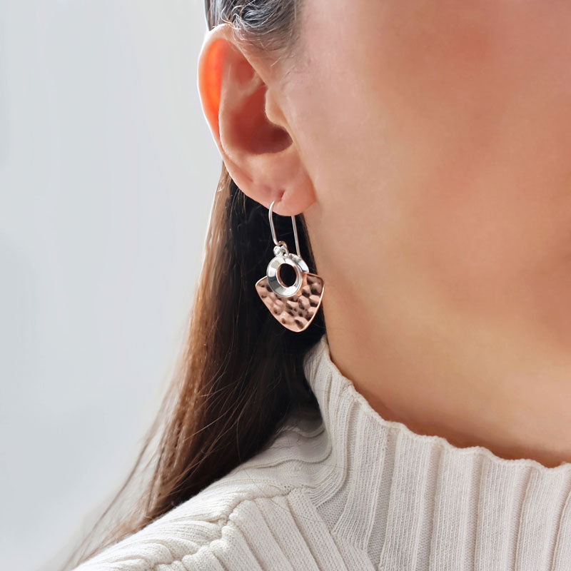 Woman in a cream turtleneck top wearing a large hammered copper and 925 silver designer mixed metal dangling earring.