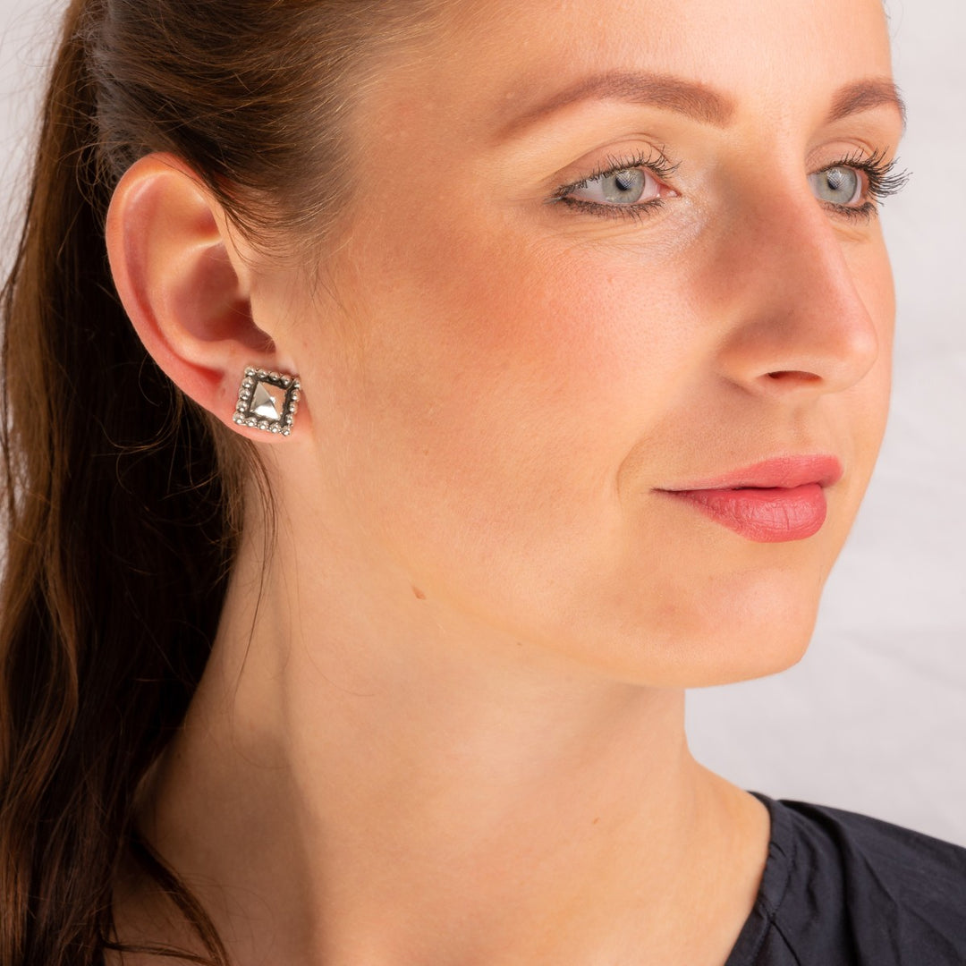 A woman wearing a black blouse with a single square silver earring in the shape of a pyramid.