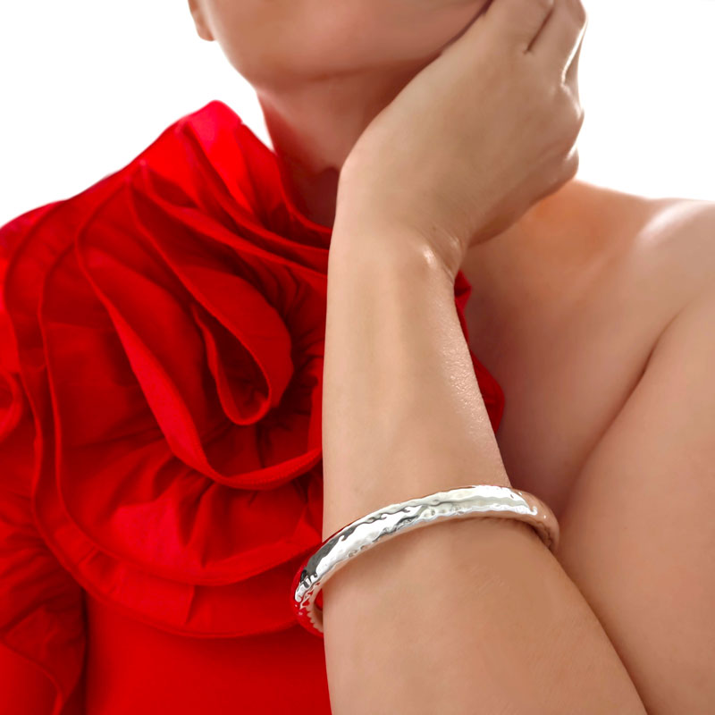 Woman in a red dress wearing a chunky sterling silver tube bangle with a hammered finish