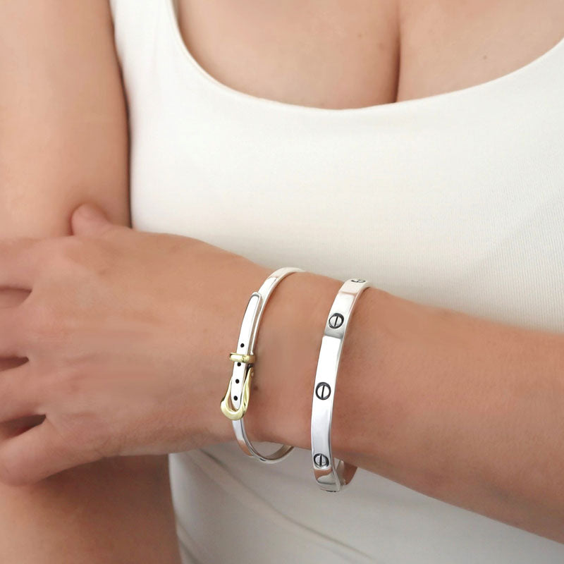 Stack of two bracelets in sterling 925 silver, one with gold accents, one with screw detail, worn on a woman’s wrist against a cream top.
