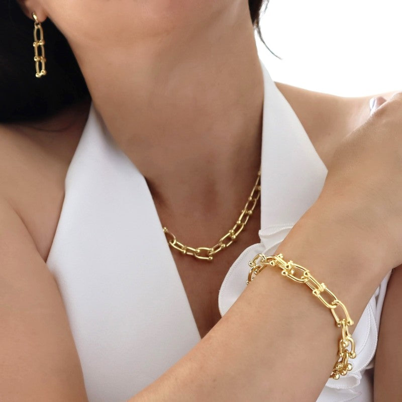 A woman in a white top wearing a gold gauge link chain bracelet and matching necklace and earrings.