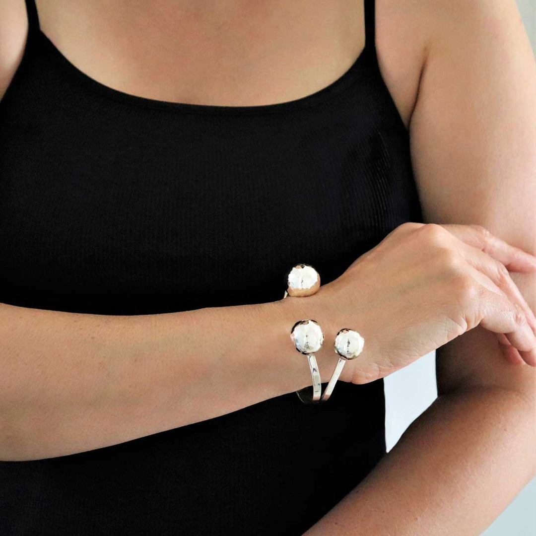 A woman in a black top wearing a silver bracelet cuff with a front opening embellished with large hammered ball beads.