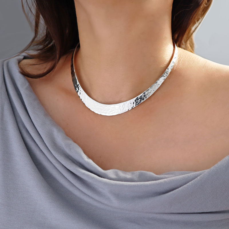 A large hammered 925 sterling silver heavy choker necklace worn by a woman in a grey dress.