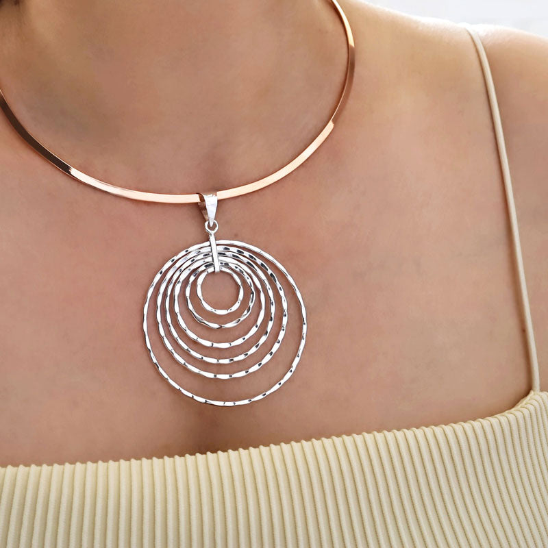 A large mixed metal sterling silver circle pendant on a solid copper choker with a polished finish worn by woman in a yellow top.