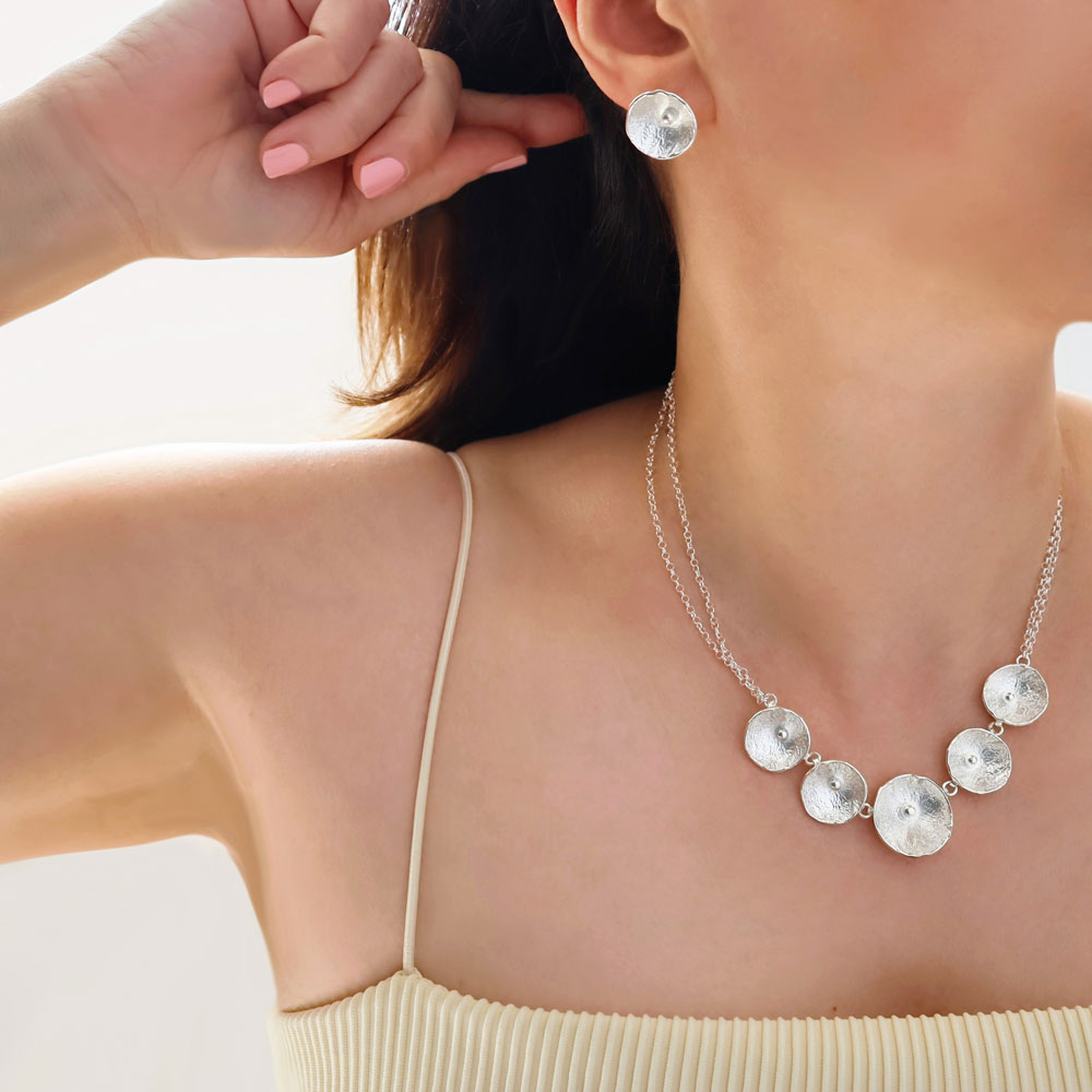 A large poppy flower statement sterling 925 silver necklace and matching earrings worn by a woman with dark hair.