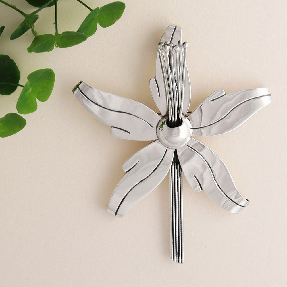 A large orchid flower pendant necklace for women in 925 sterling silver next to a cluster of green eucalyptus leaves on a beige background.