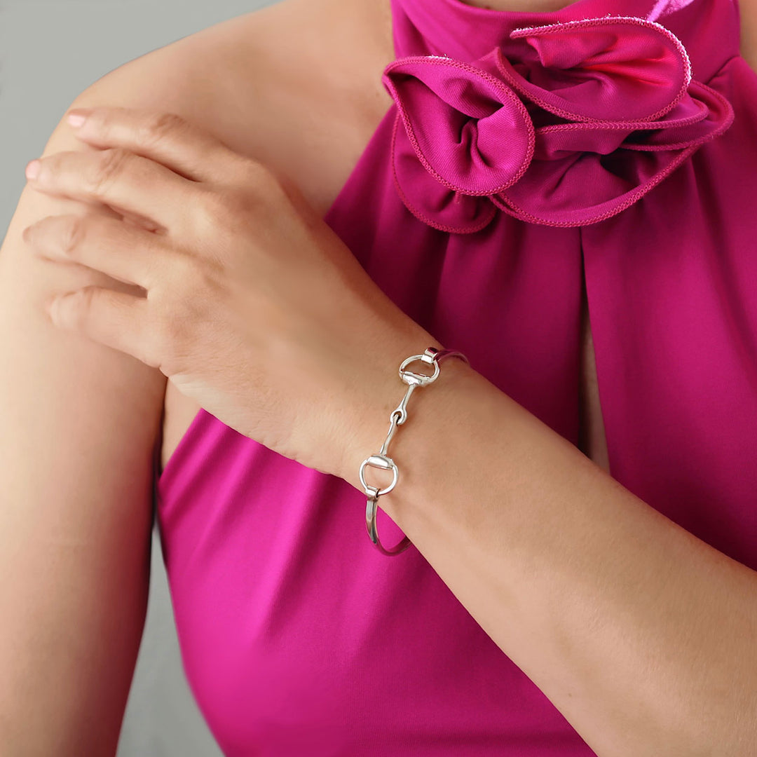 Slender sterling silver double snafflebit bangle bracelet worn by a woman in a pink dress.