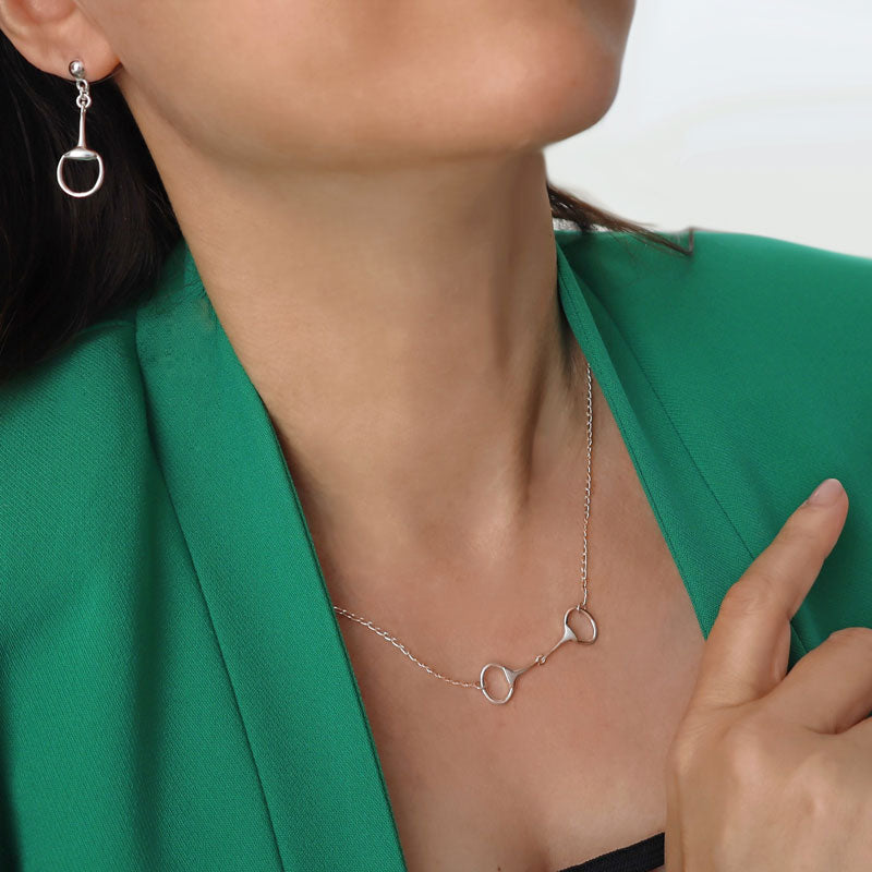 Horsebit snaffle 925 silver dangling earrings and matching pendant and chain necklace worn by a woman in a green jacket