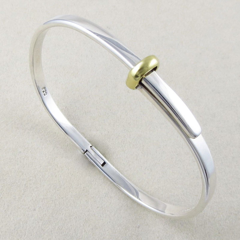 A UK hallmarked sterling 925 silver oval polished bracelet with a gold-coloured accent on a blurred background. 