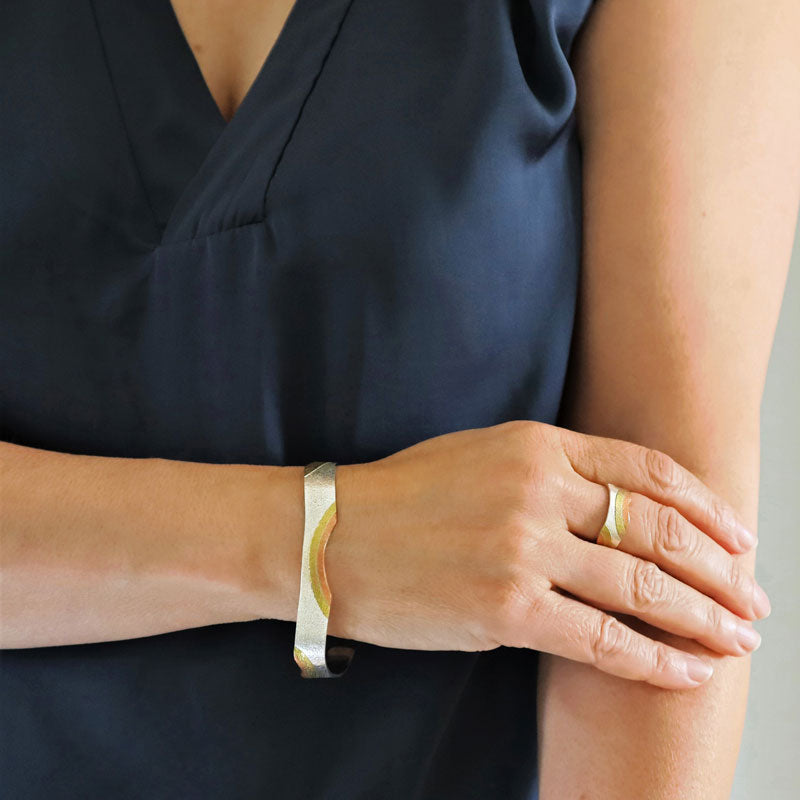 A tri-metal sterling silver, copper and gold-coloured brass adjustable bracelet and matching ring worn by  woman in a blue blouse