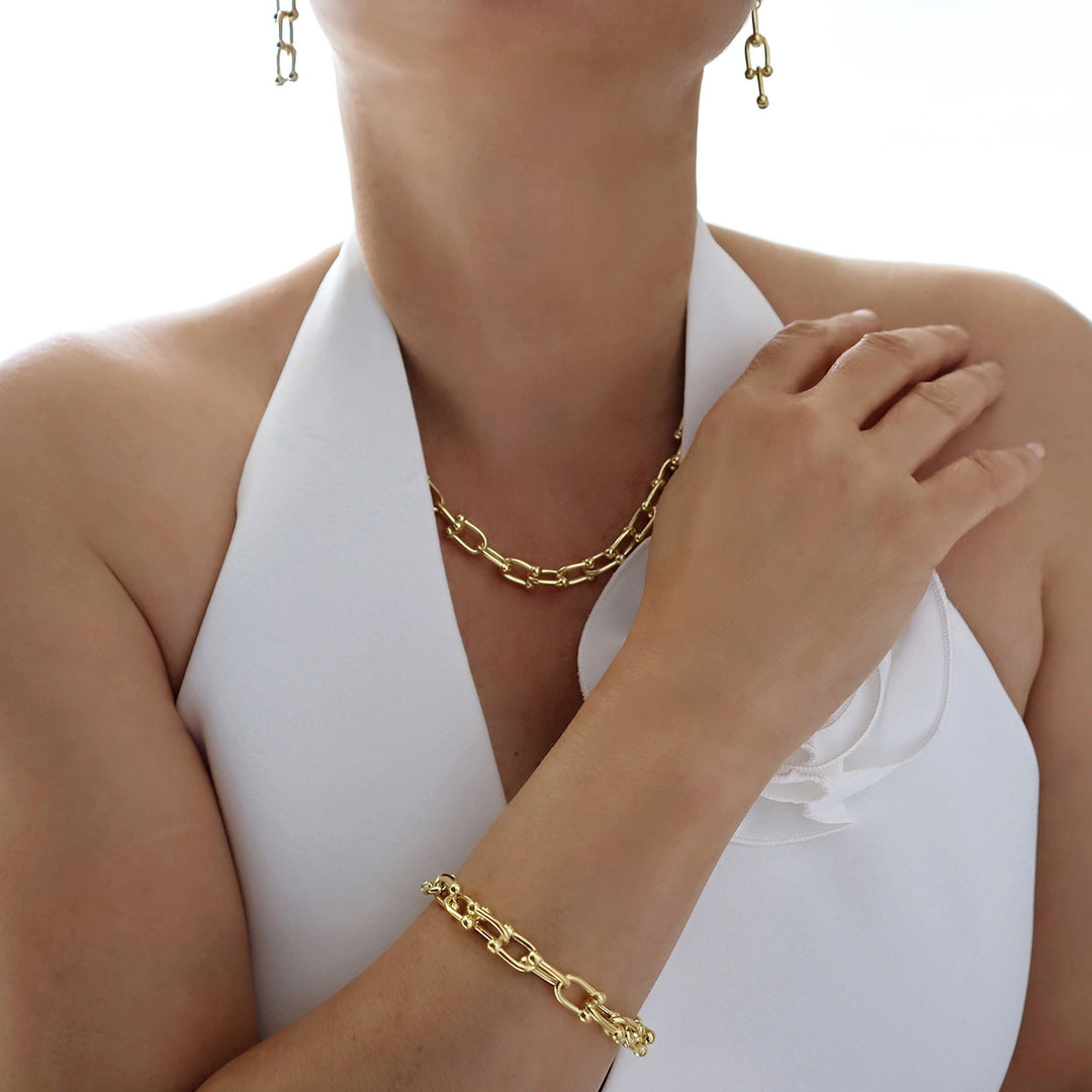 A gauge link yellow gold chain necklace with matching and earrings worn by a woman in a white top