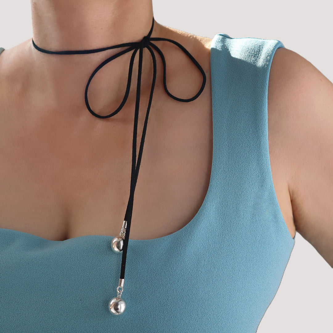 : Black suede cord necklace with sterling silver balls on the end tied in a bow around a woman’s neck wearing a blue top