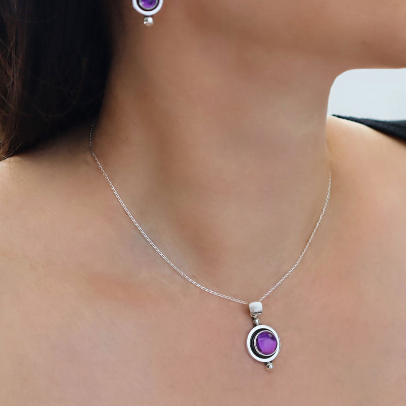 Woman with dark hair wearing a Mexican artisan 925 sterling silver pendant and chain necklace with a large purple amethyst natural gemstone and matching earrings.