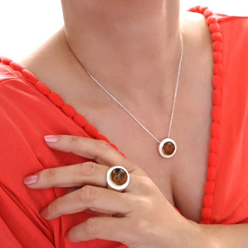 Woman wearing an orange dress and a unique UK hallmarked 925 sterling silver pendant and chain necklace decorated with a large amber gemstone cabochon and a matching ring.