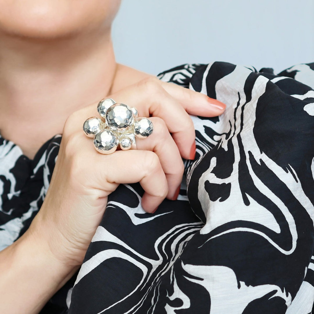 A woman in a black and white dress wearing a large sterling silver cocktail bubble ring with clusters of hammered ball beads.