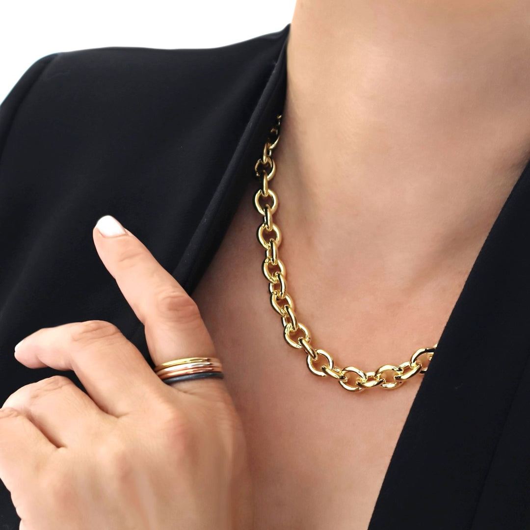 A person wearing a chunky gold chain necklace with a stack of mixed metal band rings on a finger in silver, copper and gold.