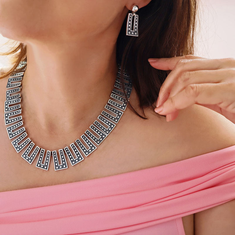 A large Margot de Taxco domino link statement sterling silver necklace and matching earrings worn by a woman in a pink off the shoulder top