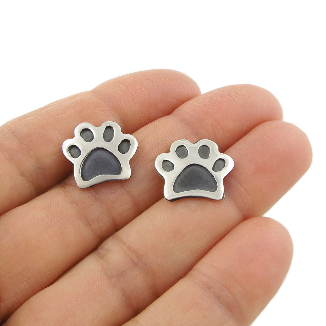 Sterling 925 silver dog or cat paw print stud earrings held between fingers on a white background