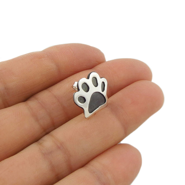 925 silver paw print stud earring for women held between fingers on a white background