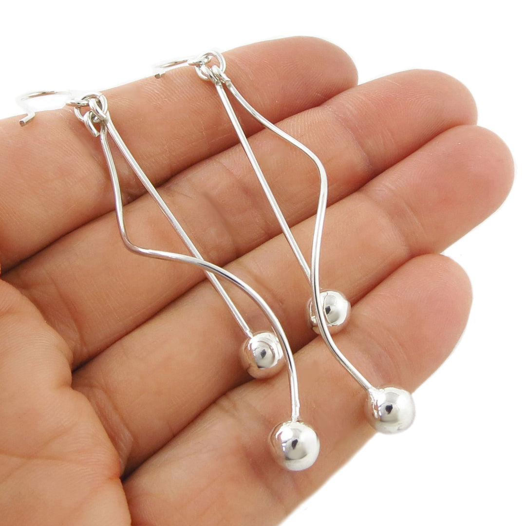 Sterling 925 Silver spiral drop errings with ball beads held in a hand against a white background