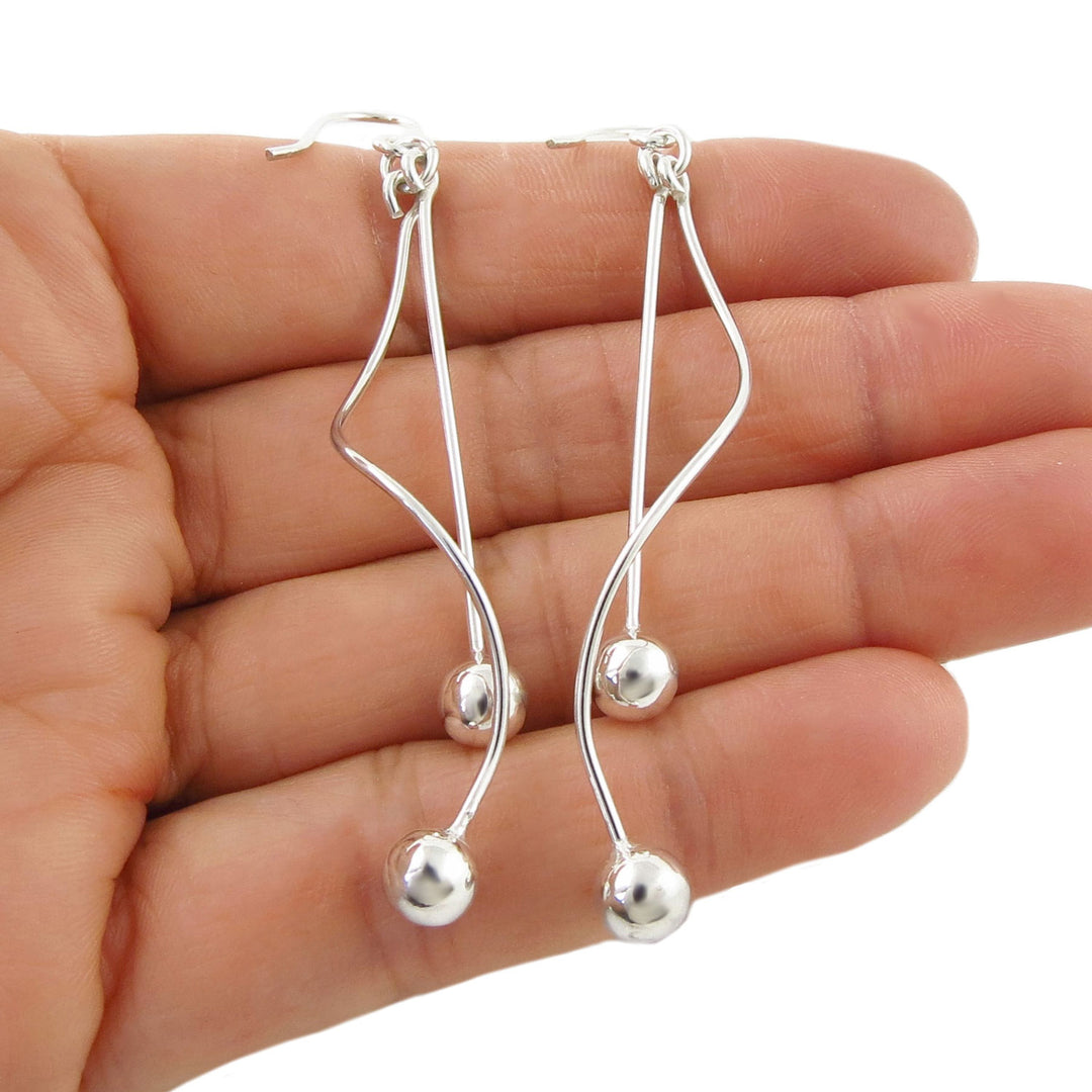 925 sterling silver dangling stick and spiral earrings with bal bead ends held in a hand against a white background