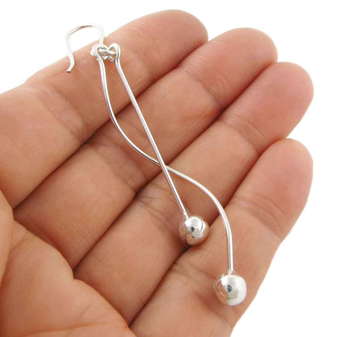 Sterling 925 ilver spiral stick drop earring with ball beads held between fingers on a white background