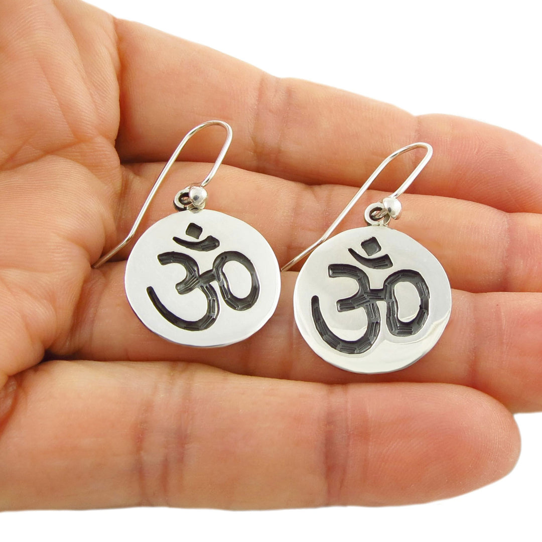 Sterling 925 Silver Om symbol dangling drop earrings held in a woman's hand against a white background