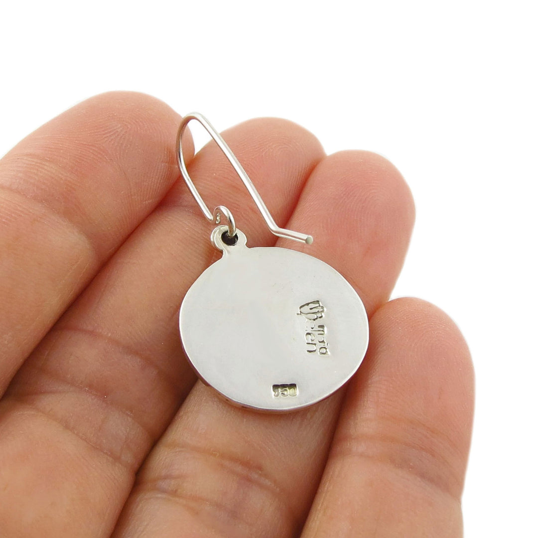 Handmade Maria Belen Nilson 925 Mexican Silver earring held upside down to show the hallmark between fingers on a white background