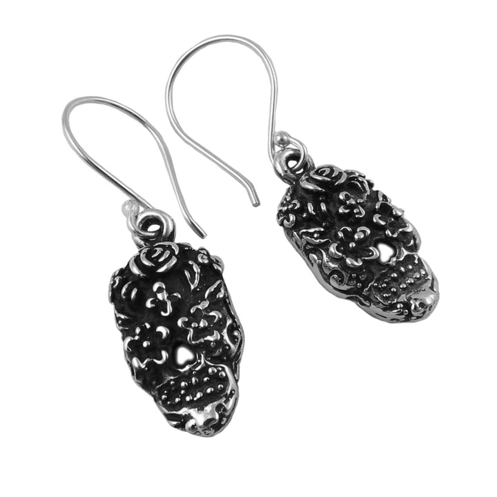 Pair of silver sugar skull earrings with intricate designs on a white background