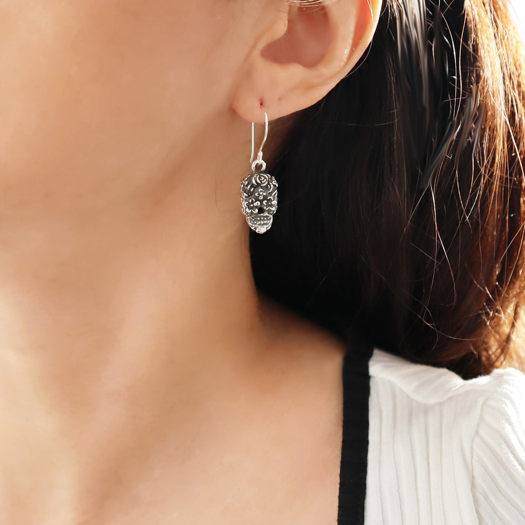 Close-up of a silver sugar skull earring worn by a woman with a blurred background