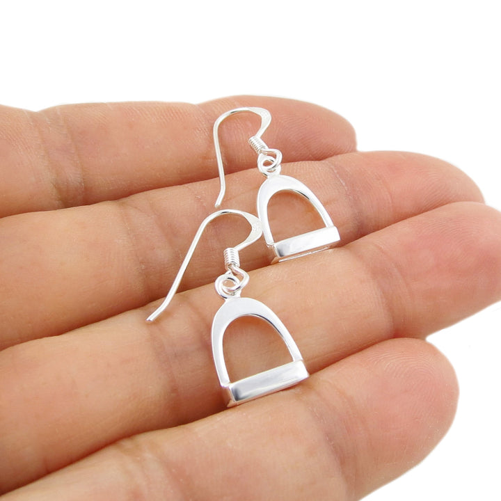 925 silver equestrian horse stirrup earrings for women held between fingers on a white background