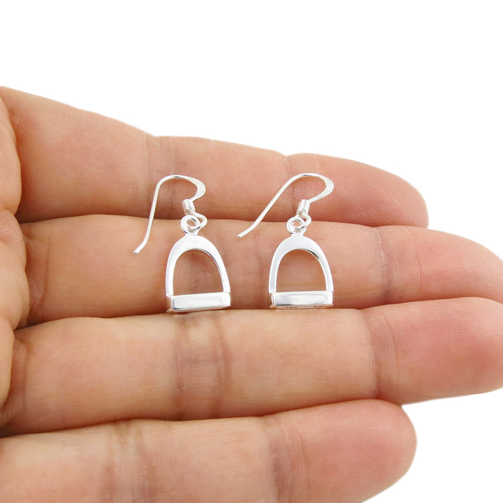Sterling 925 silver equestrian horse stirrup earrings for women held between fingers on a white background