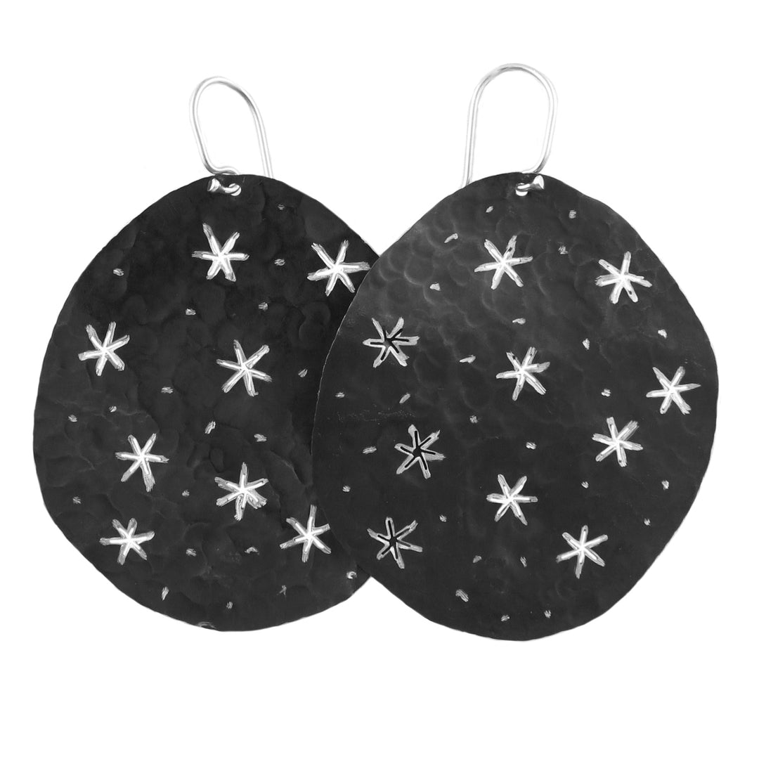 Large round silver earrings with blackened niello with white star patterns on a white background