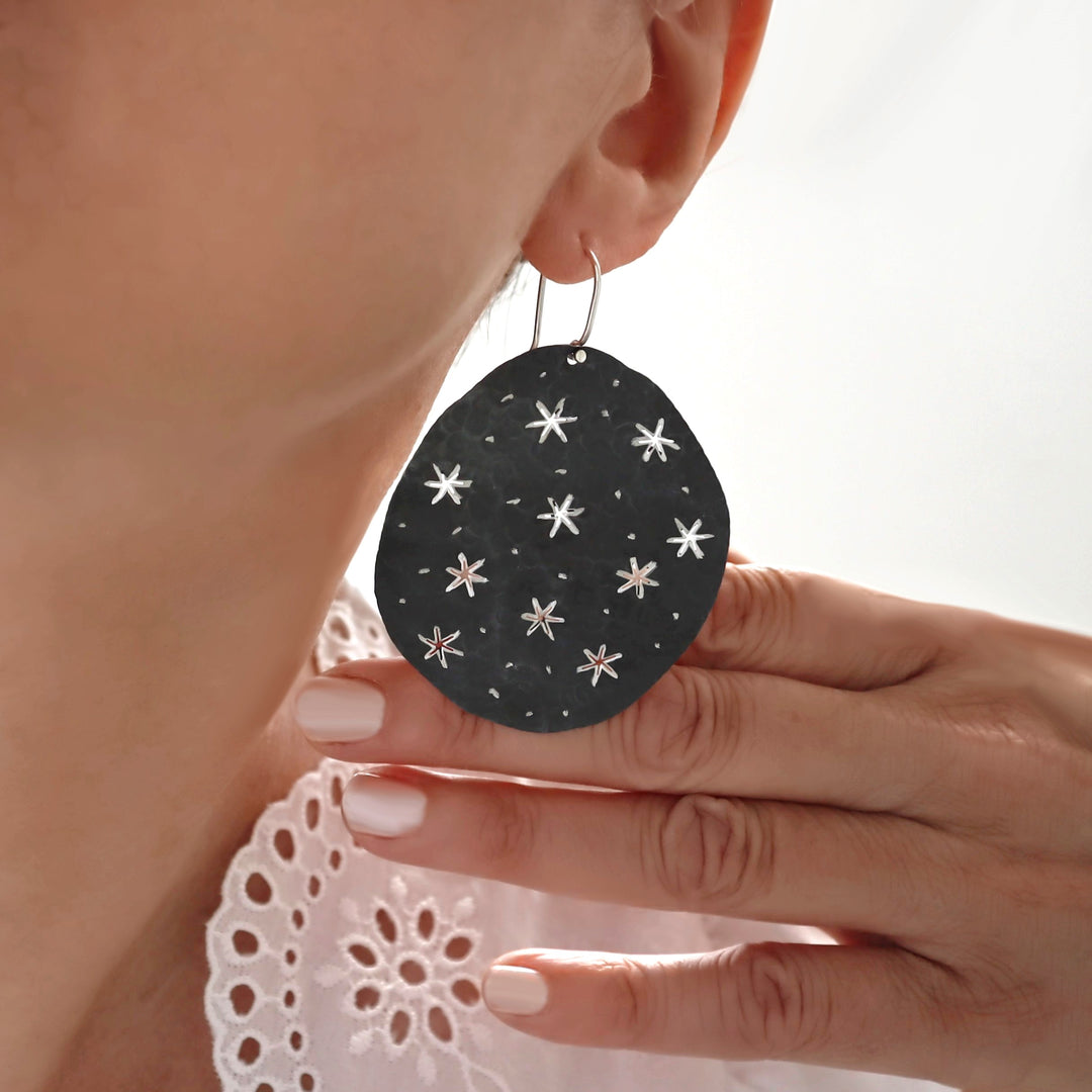 Large silver earrings with a black finish and shiny star pattern worn by a woman. 