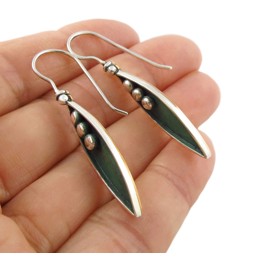 Sterling 925 Silver and green leaf-shaped drop earrings with silver ball beads held in a hand against a white background