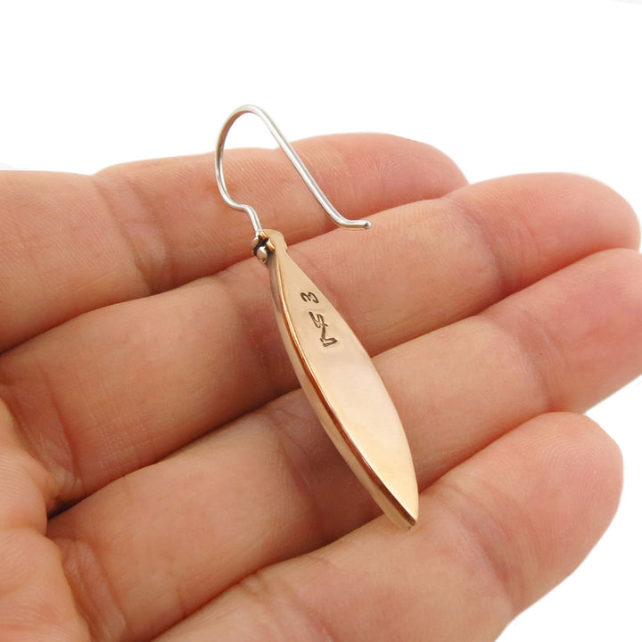 Copper and 925 silver mixed metal  leaf-shaped earring held in a hand to show the silversmith's signature against a white background