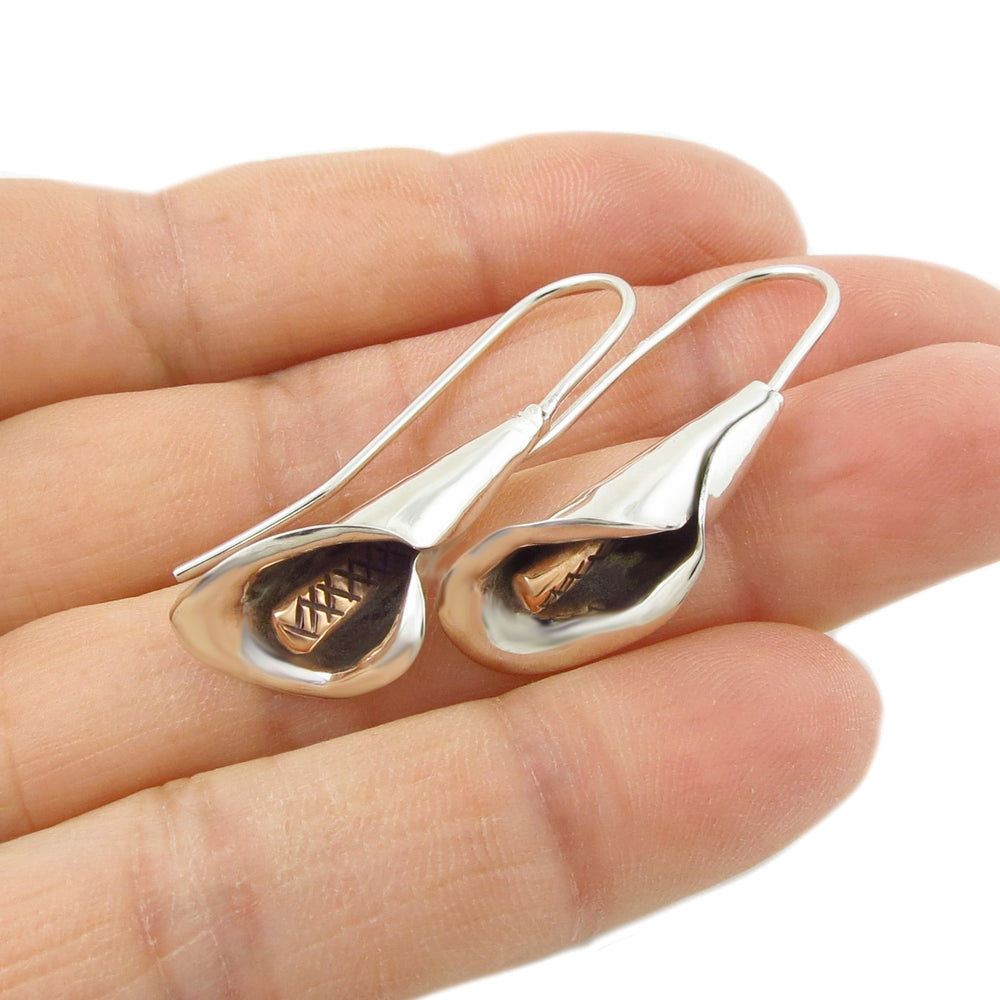 Silver calla lily flower earrings with copper accents held between fingers on a white background