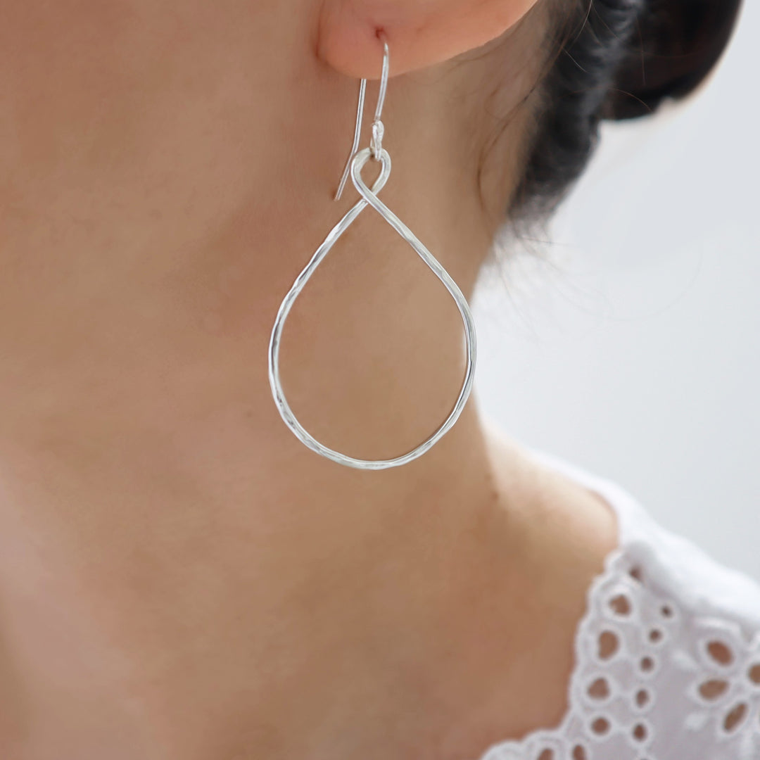 Silver hoop earrings worn by a woman with a blurred background