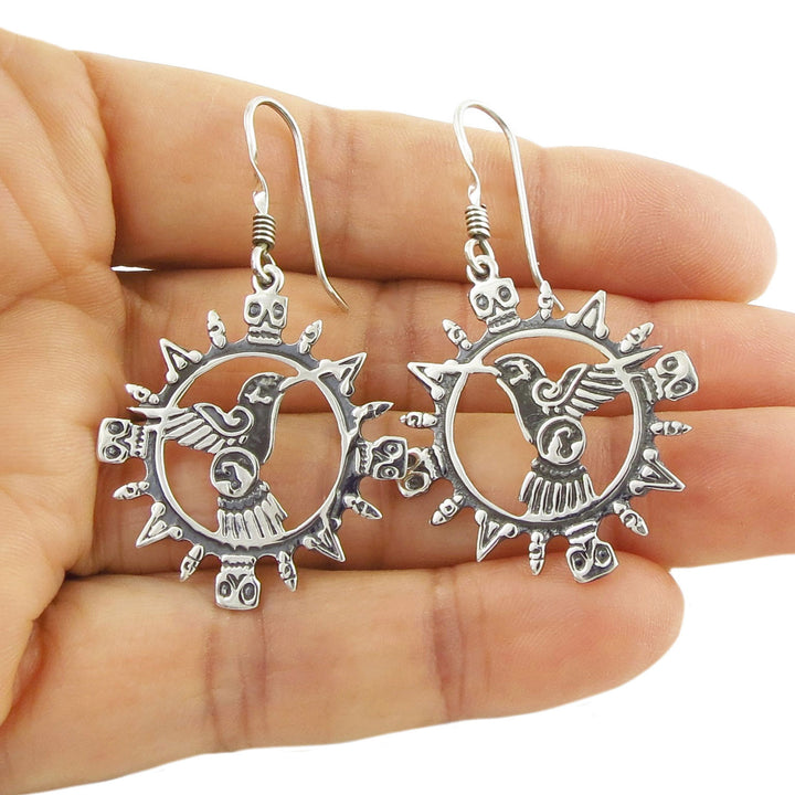 925 sterling silver Mexican Aztec hummingbird and skull earrings held in a hand against a white background