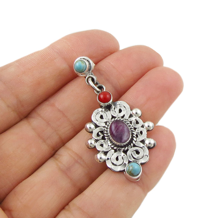 A single 925 sterling Silver earring with amethyst and turquoise gemstones held in a hand on a white background